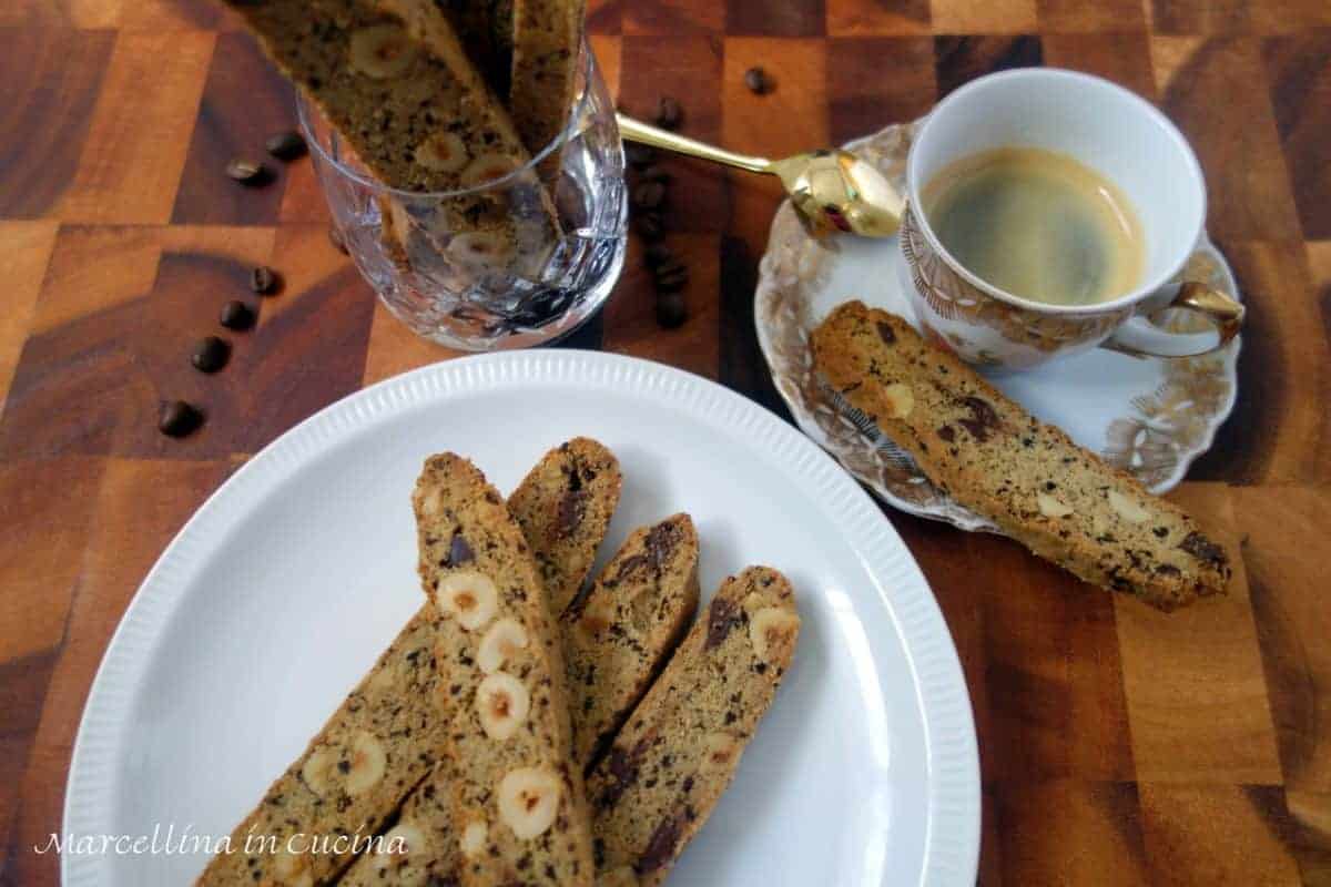 biscotti with nuts and chocolate on white plate with gold spoon, espresso cup and coffee beans.