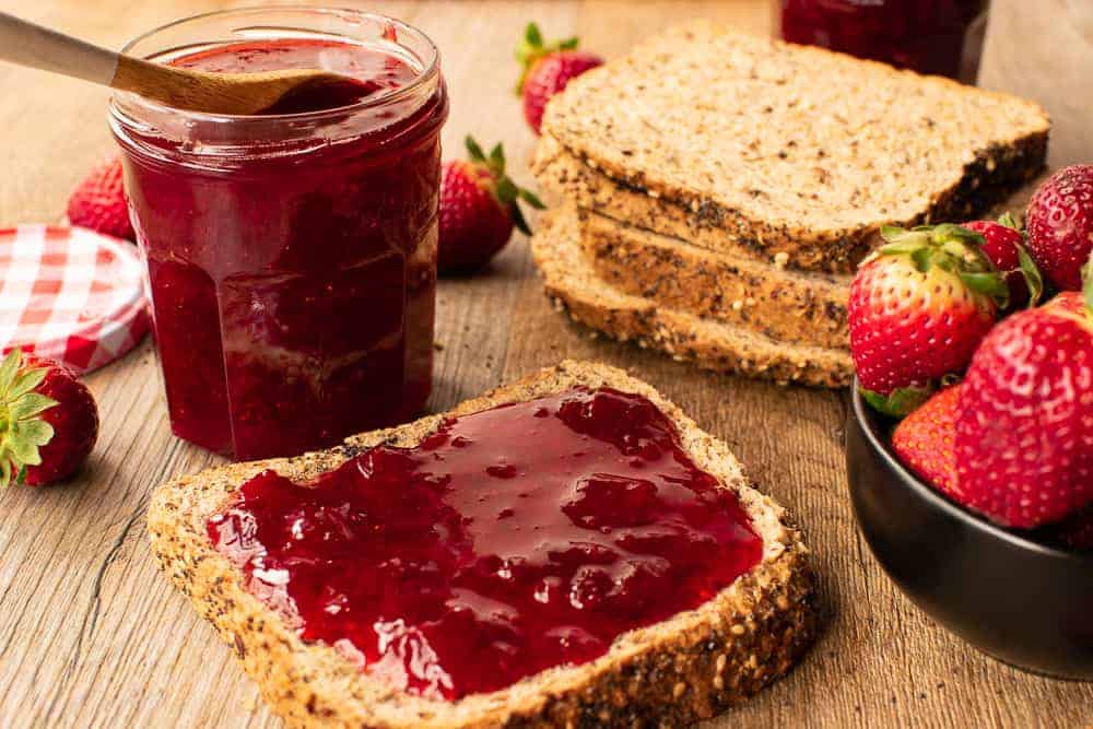 Bread served with the preserves and a jar on a wooden table.