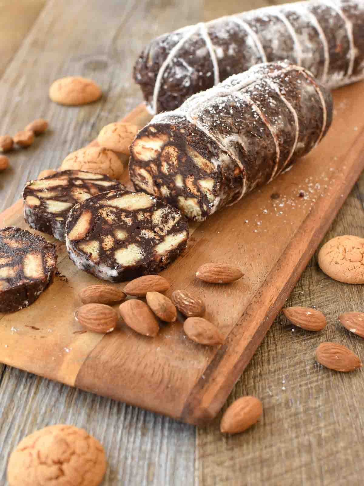 Chocolate salami on wooden board with three slices cut.