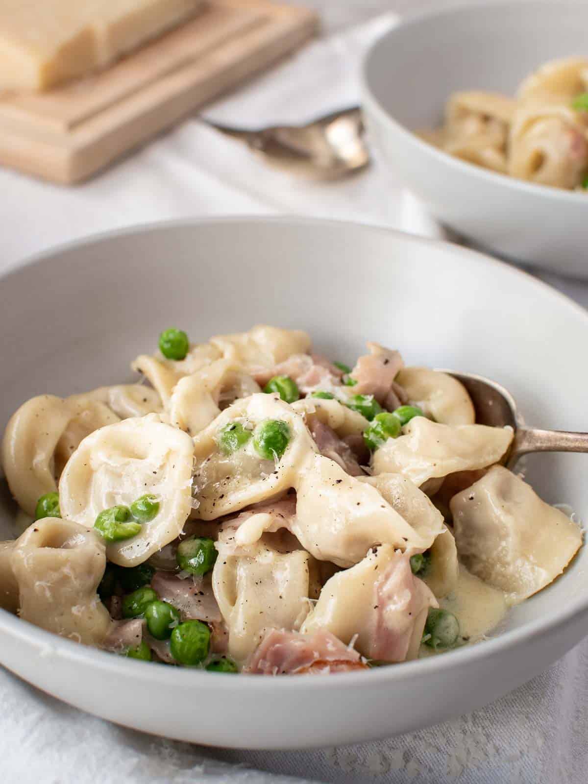 bowl of tortellini with peas and ham.