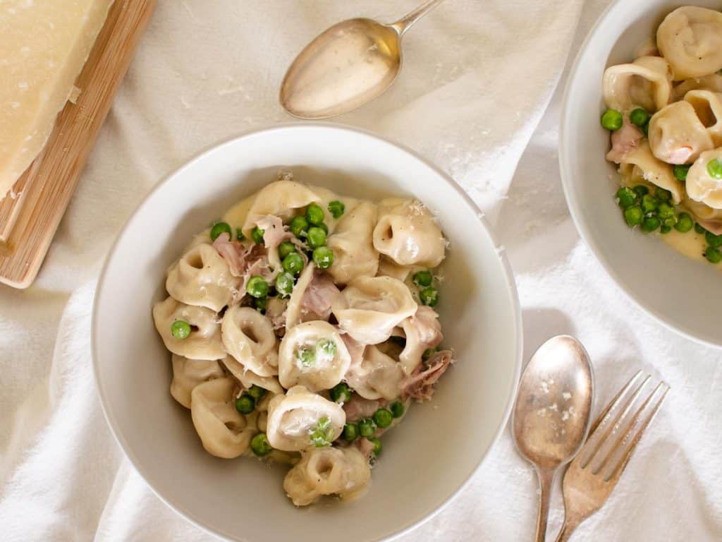 tortellini with cream, peas and ham in a bowl viewed from above.