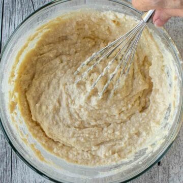 Lumpy batter in a glass bowl being mixed with a whisk.