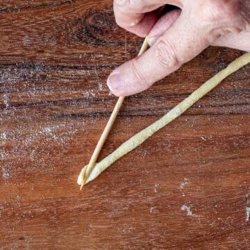 A bamboo skewer pressed into the end of a strand of dough.