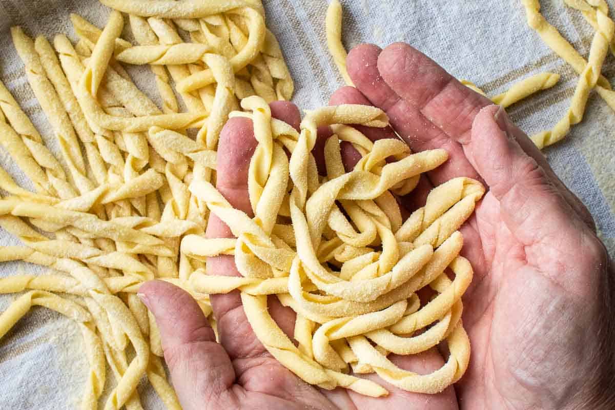 Pile of twirled, handmade pasta in cupped hands with more pasta nearby.