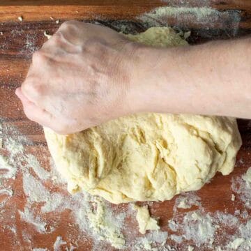 A hand kneading yellow pasta dough.