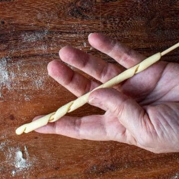 Dough wound around a bamboo skewer being displayed on an open hand.
