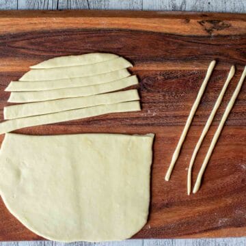 Oblong sheet of rolled dough cut into thick strips with three strands of dough nearby.