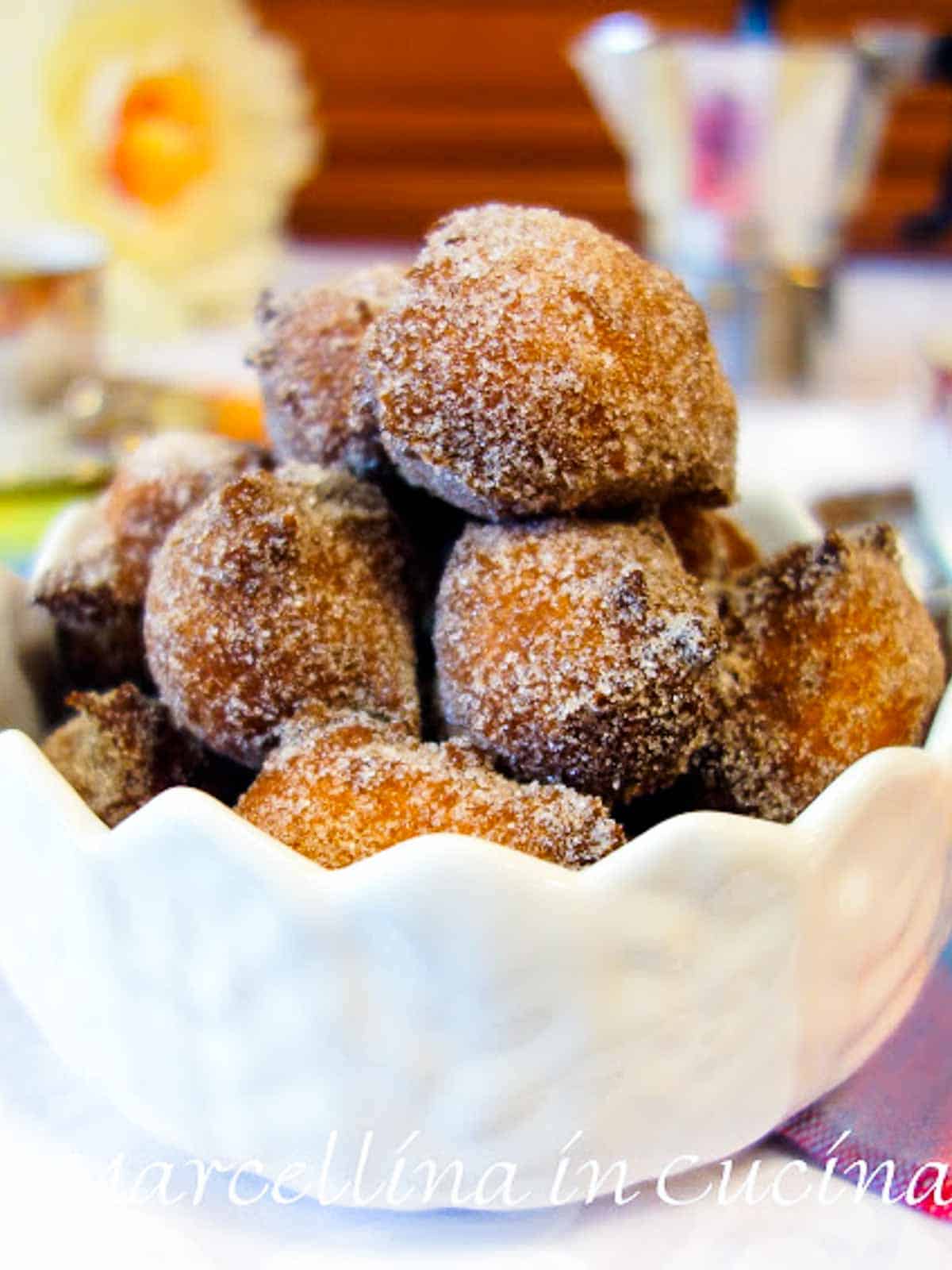 pile of fried dough balls coated in cinnamon sugar in a white bowl.