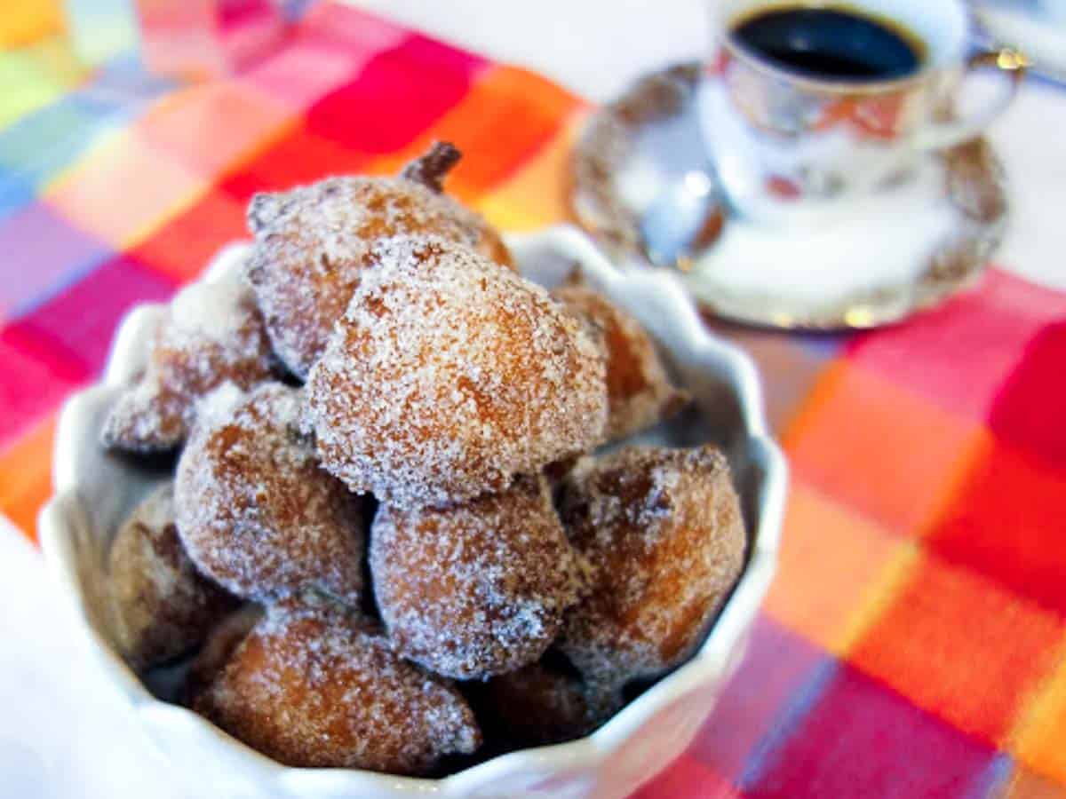 fried dough balls in white bowl with coffee cup in the background.