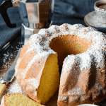 Lemon Yogurt cake with slice in the front and two espresso cups of coffee and moka pot
