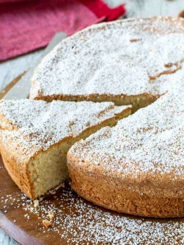 Italian Almond Cake on round wooden board with one wedge cut.