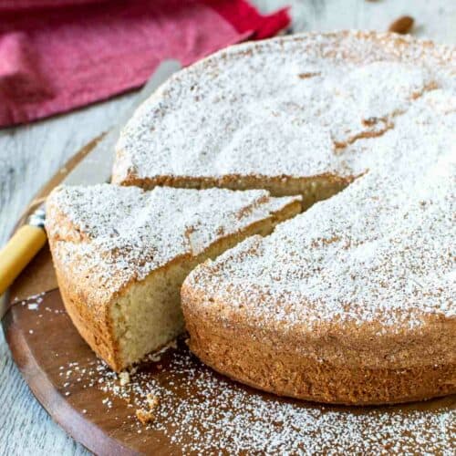 Italian Almond Cake on round wooden board with one wedge cut.