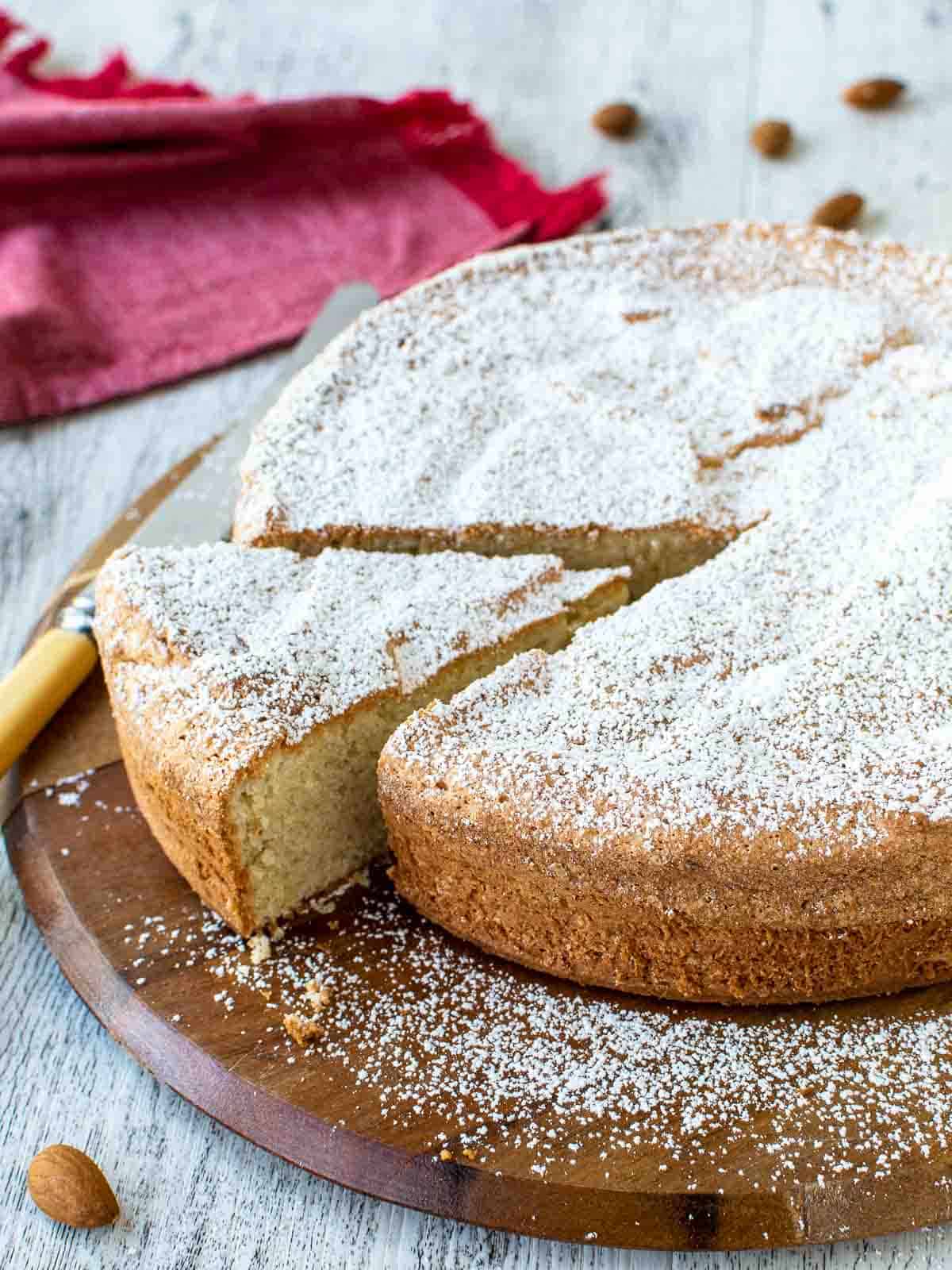 Italian Almond Cake on round wooden board with one wedge cut.