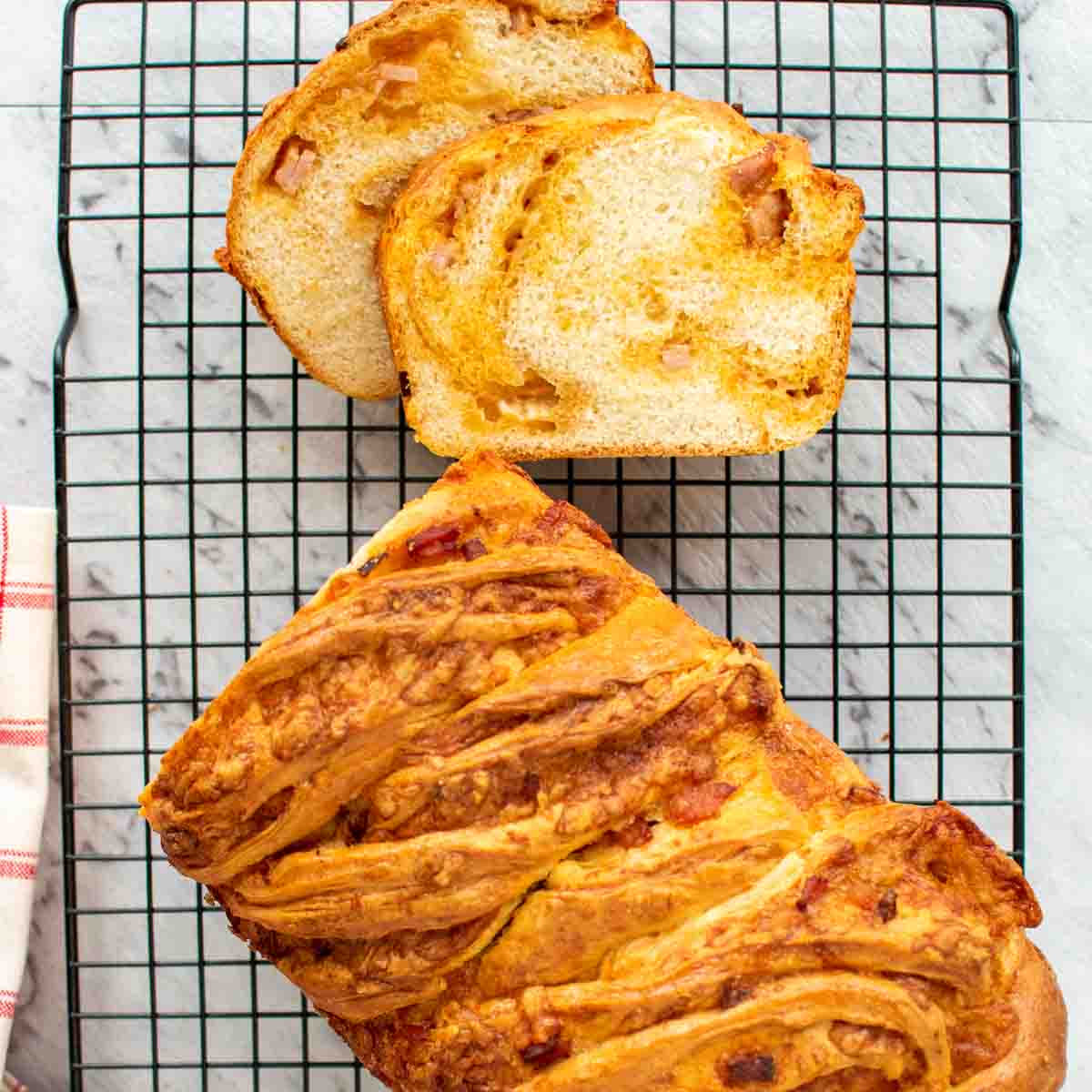Bread loaf on black wire rack with two slices cut viewed from above