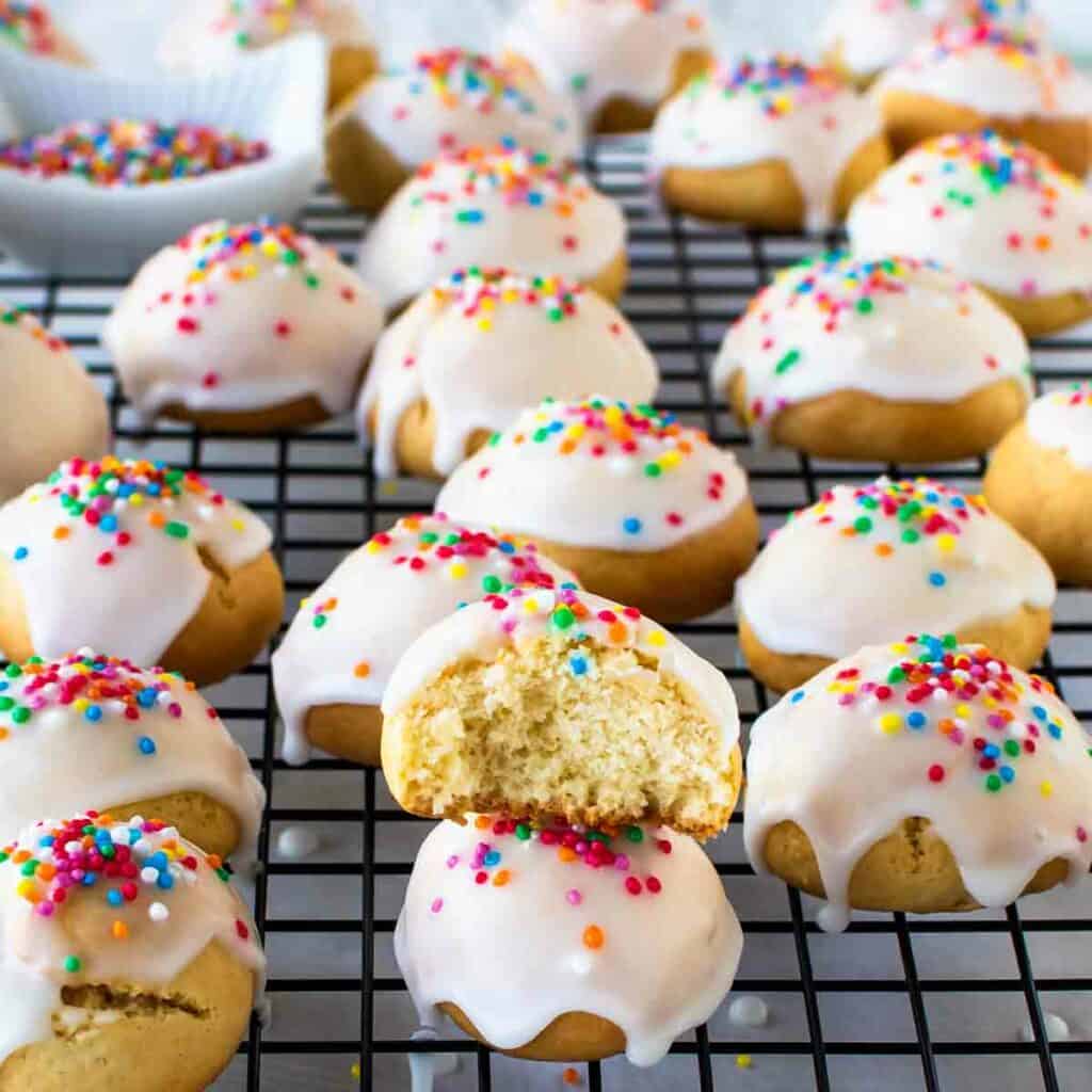 Italian Anise Cookies on black wire rack with one stacked cookie with bite taken.