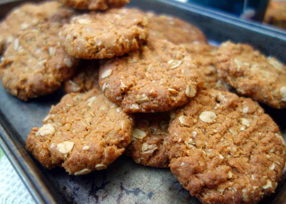 Close up of Anzac Biscuits on dark coloured baking tray