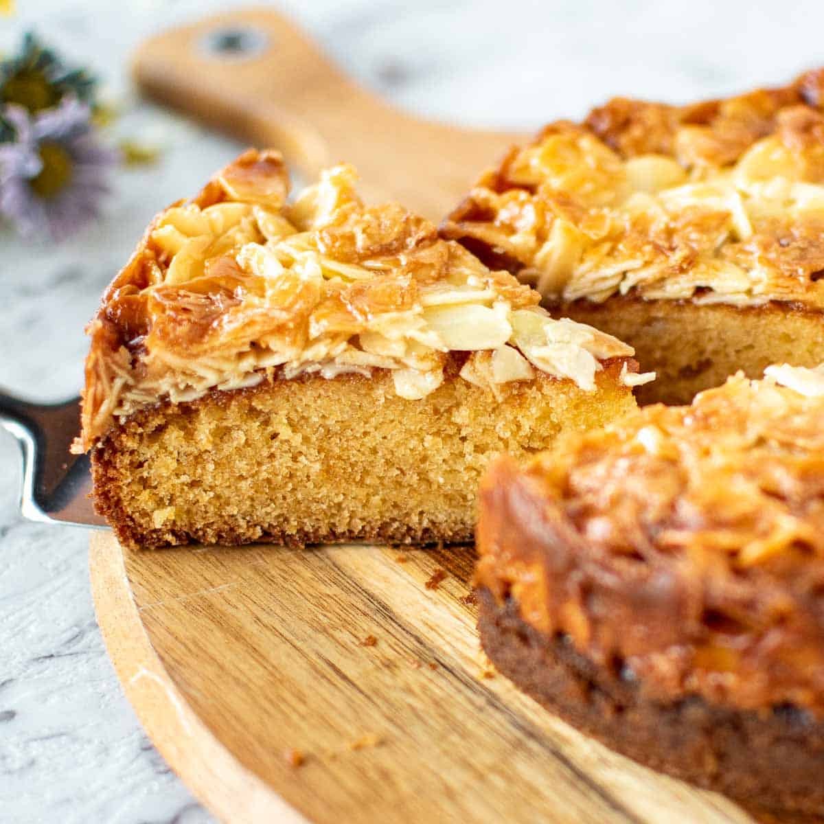 slice of cake with almond topping cut from whole cake viewed side on.