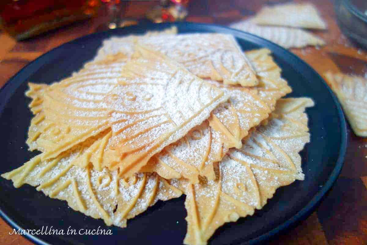 pizzells dusted with powdered sugar on a black plate.