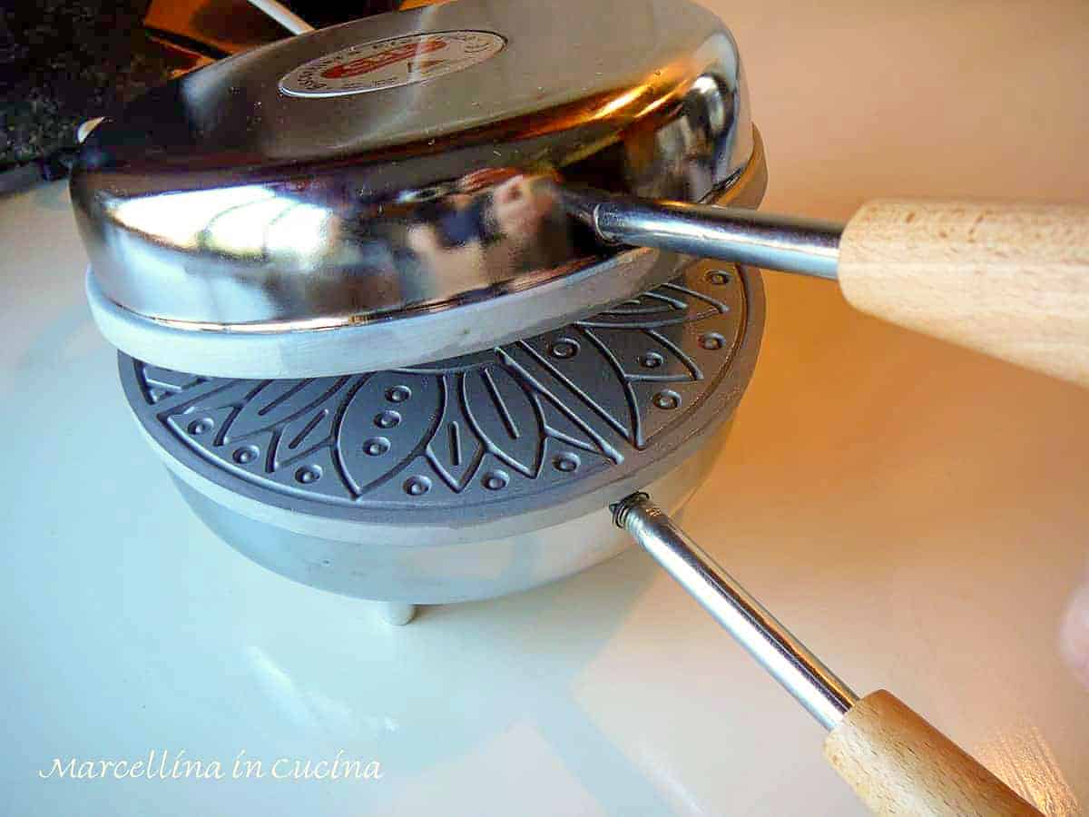 a stainless steel pizzelle iron partially opened showing the griddle inside.