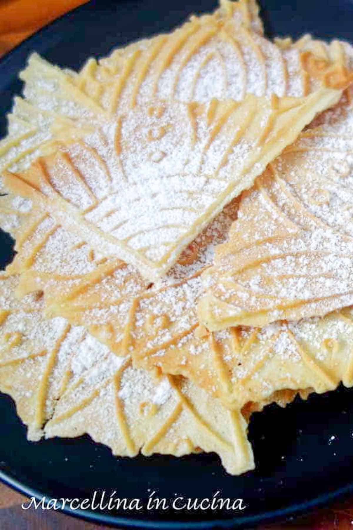 Lemon pizzelle dusted with powdered sugar on a black plate.
