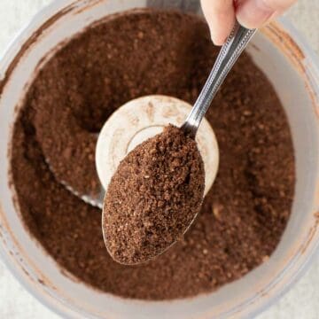 Brown crumbly mixture in a spoon with more in food processor below.