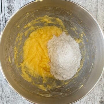 Flour on top of creamed butter in a stainless steel bowl.