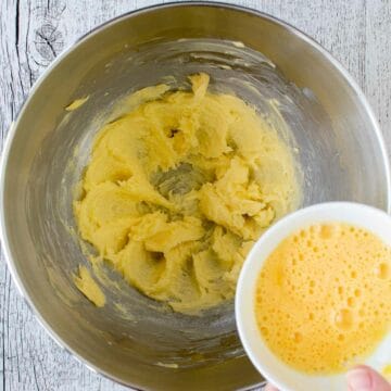 Creamed butter in a stainless steel bowl with beaten egg about to be poured in.