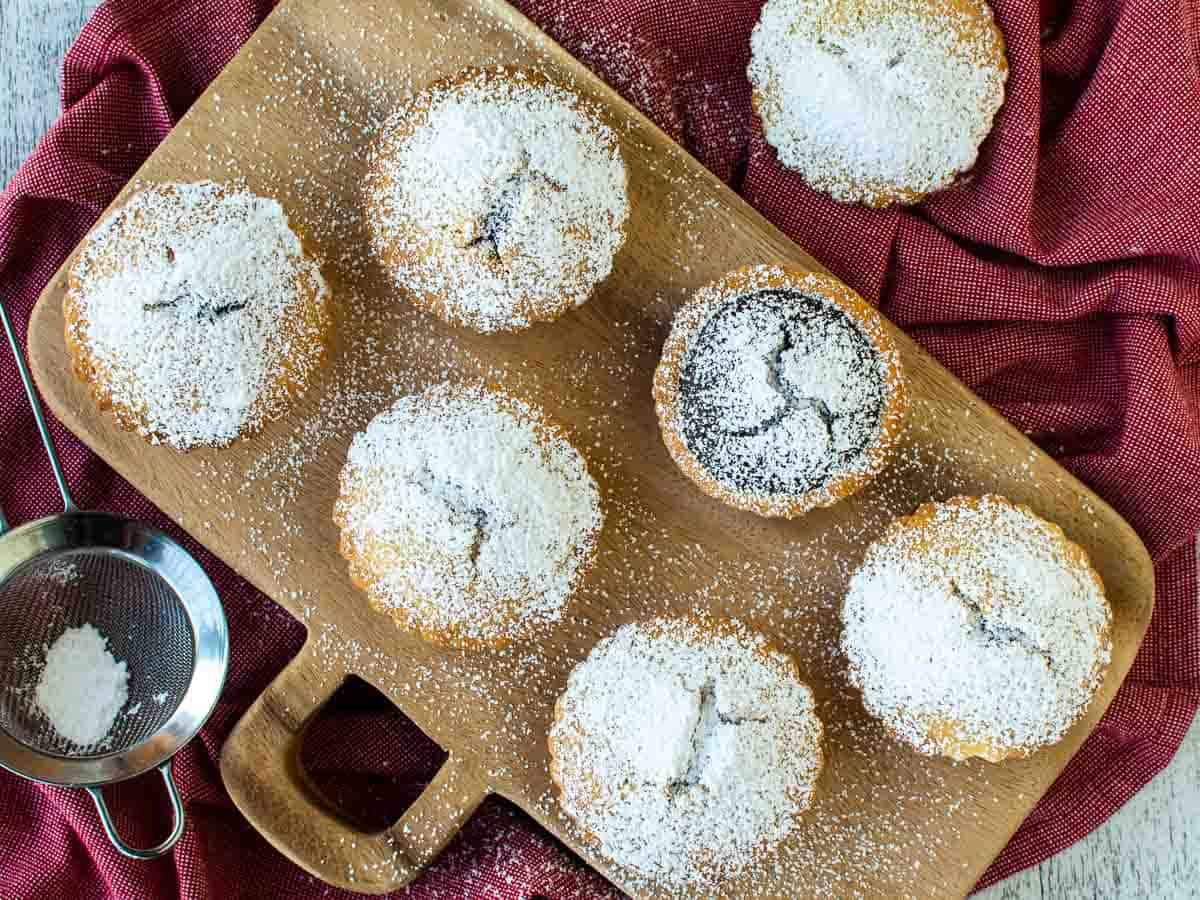 Sugar dusted small pies on a wooden board viewed from above.