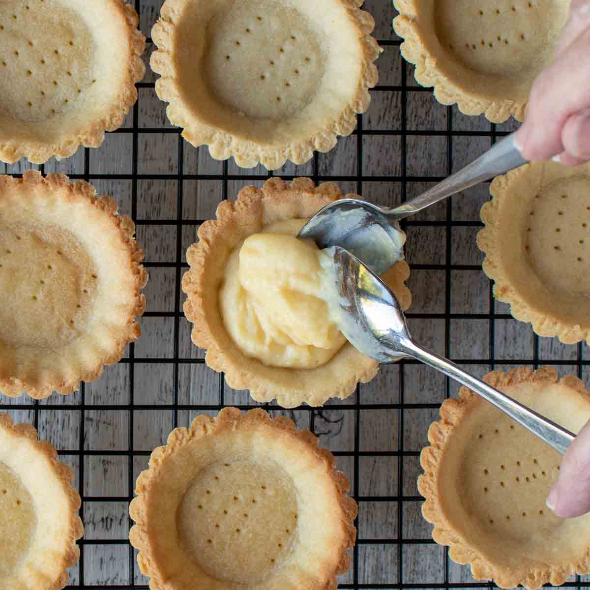 Pastry cream being spooned into tartlet bases.