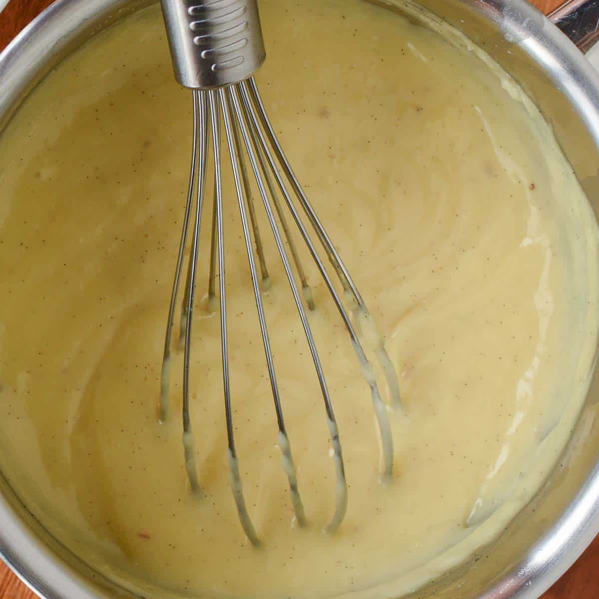 Overhead view of thickened pastry cream in a saucepan with a whisk.