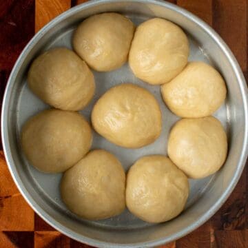 Nine balls of dough in a round cake pan.