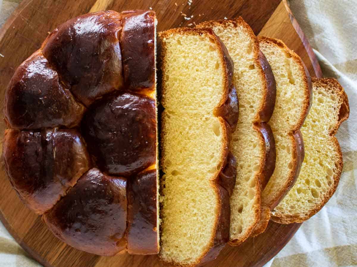 Sliced round bun loaf which has a dark glossy exterior and yellow fluffy interior.