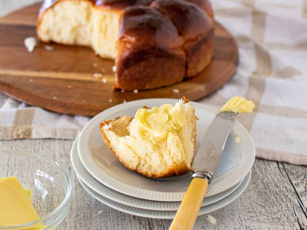 Buttered bun on white plates with whole bun loaf behind.