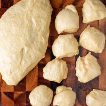 Large piece of dough and several smaller dough balls on a wooden board.