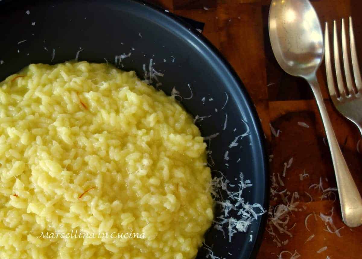 Saffron risotto with grated Parmesan cheese on a black plate with spoon and fork