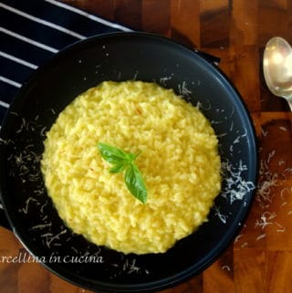 Saffron risotto with grated Parmesan cheese on a black plate with spoon and fork and black and white striped kitchen towel