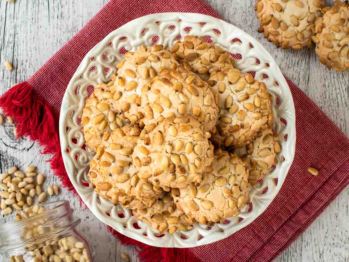 Cookies coated in pine nuts on white plate viewed from above.