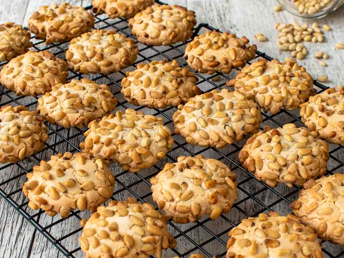 Cookies covered in pine nuts on a black wire rack.