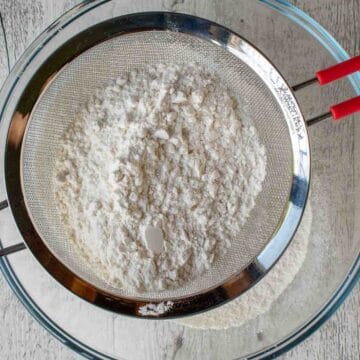 Flour in a sieve over a glass bowl.