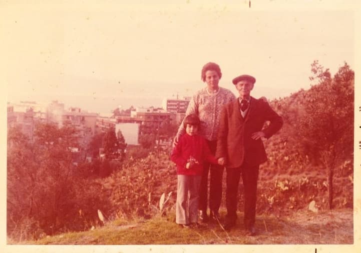 old photo of old man, woman and small child with city in the background.