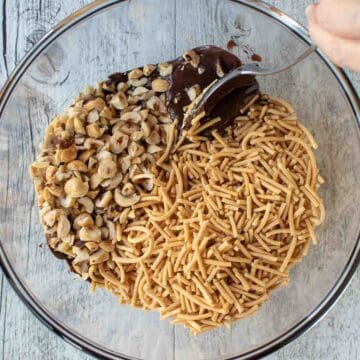 Fried noodles and chopped nuts on top of melted chocolate in a glass bowl.