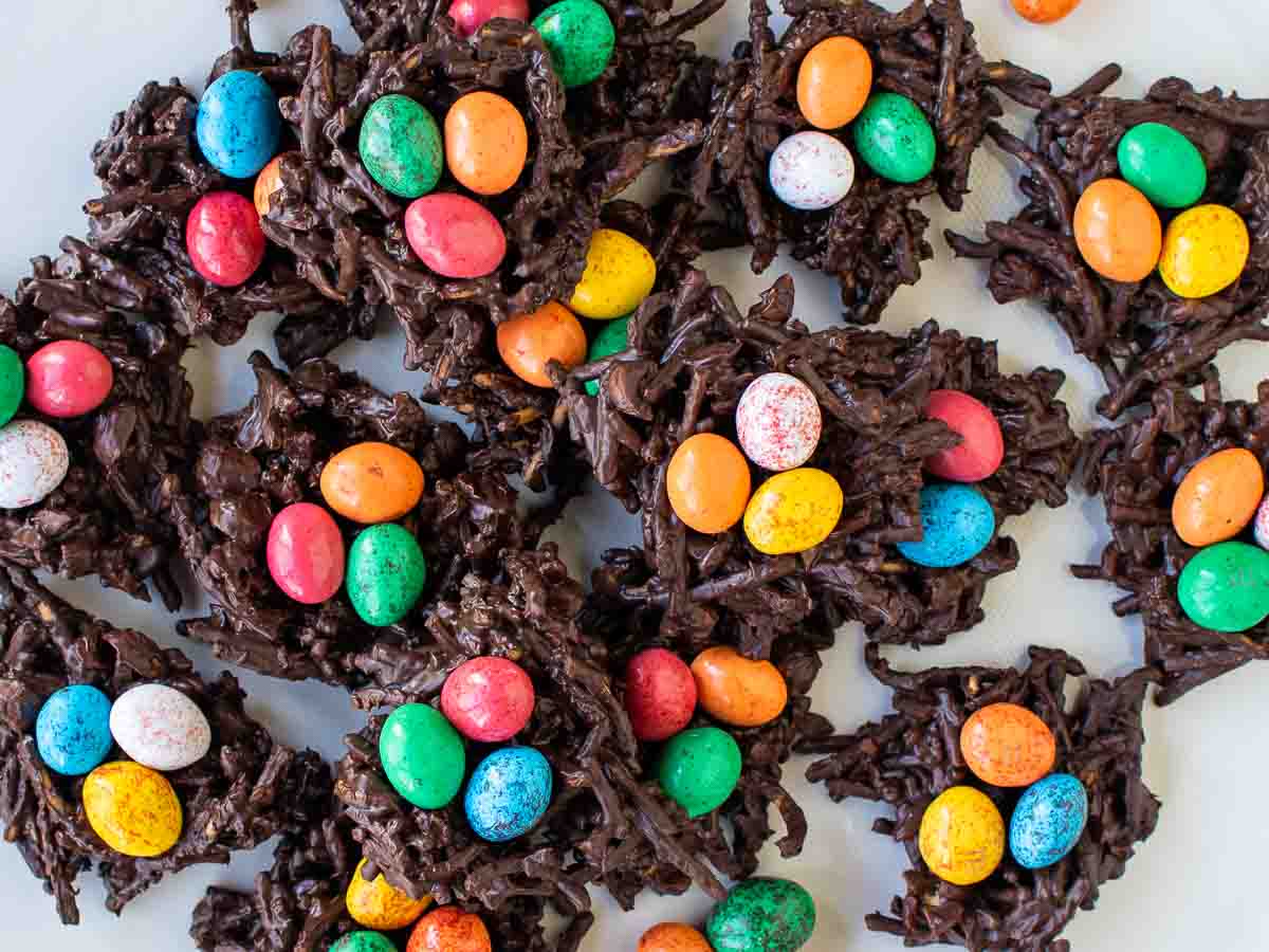 Piles of chocolate and noodles nests with candy eggs in each viewed from above.