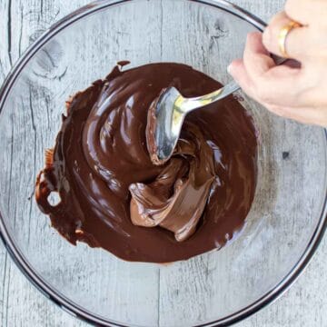 Melted chocolate and Nutella being stirred together in a glass bowl.