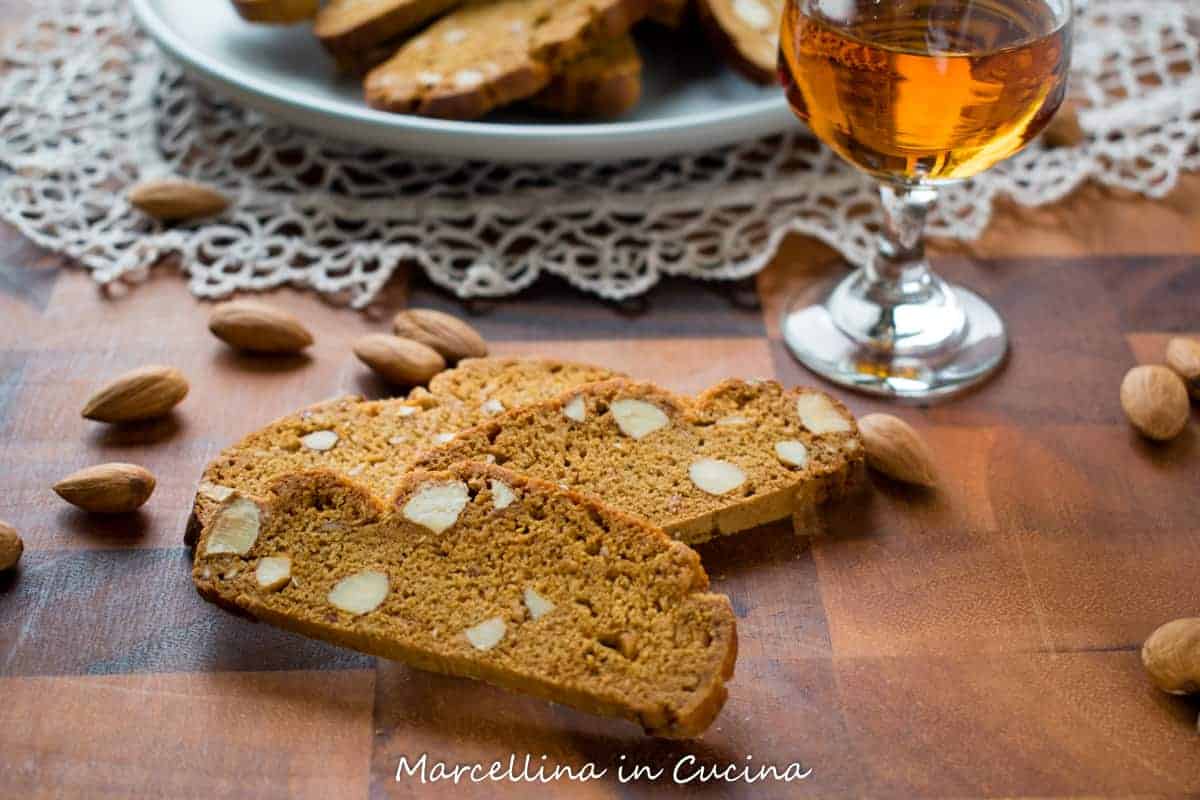 Italian Piparelli, spicy biscotti on wooden table with glass of liqueur and plate of biscotti in the background