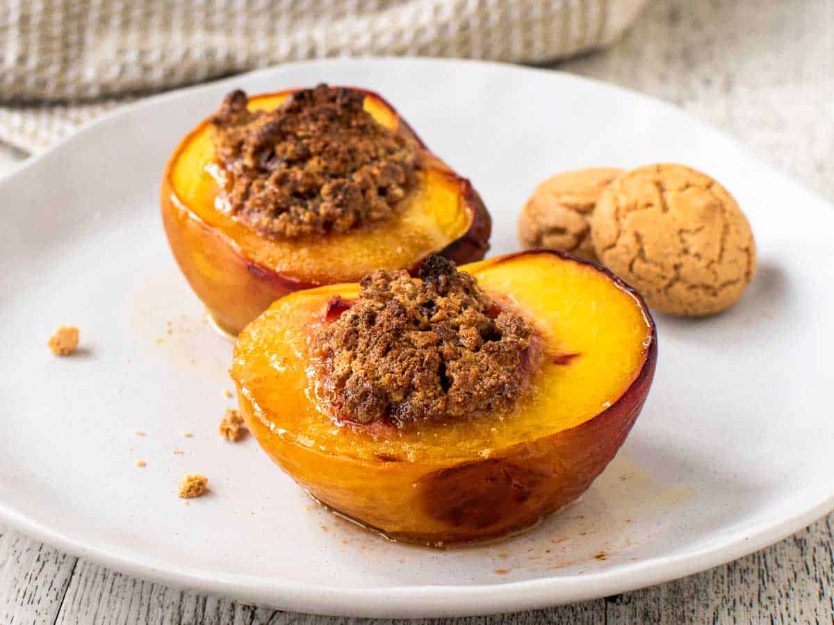 Two peach halves filled with amaretti on white plate.