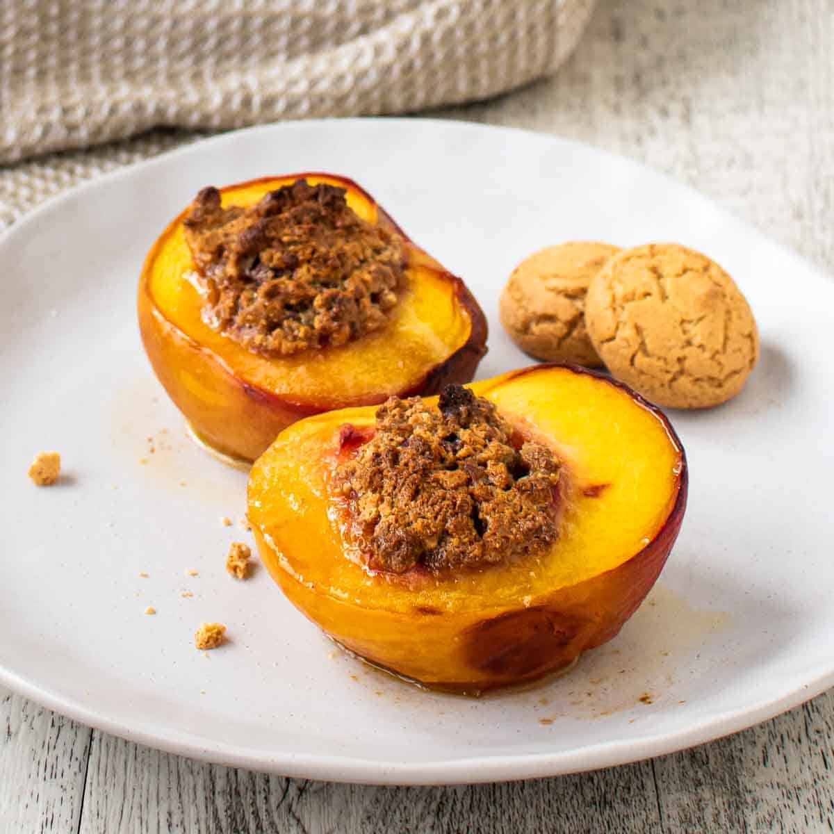 Baked Peaches on a white plate with more baked peaches in the background.