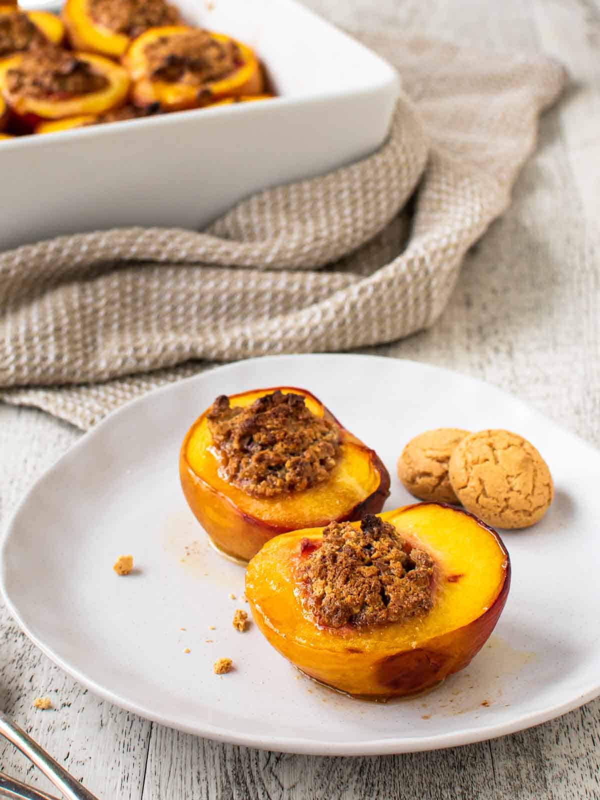 Baked Peaches on a white plate with more baked peaches in the background.