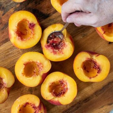 Peaches cut in half and using a teaspoon to scoop out some of the pulp.
