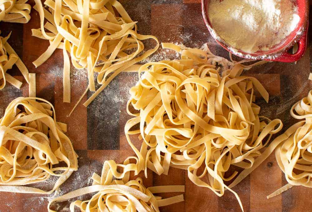 several bunches tagliatelle with small red dish of flour.