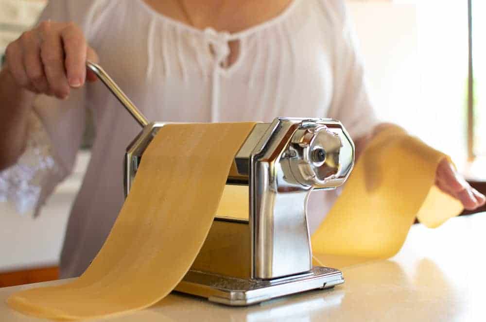Woman in white rolling pasta through pasta machine.